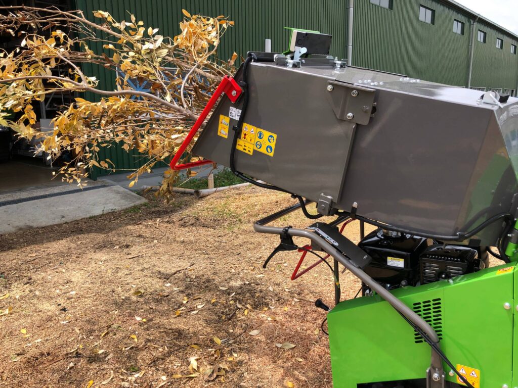 Detail photo of timber and branches loaded into an Ohashi ES101GH 4-inch Compact tracked woodchipper on some grass
